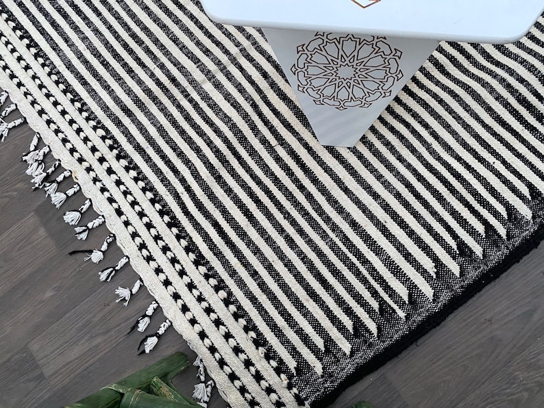 Handwoven Moroccan rug crafted from wool, designed with sleek black and white stripes in a timeless pattern (see photos). This Berber carpet embodies minimalist elegance while preserving traditional craftsmanship. Soft, durable, and fringed, it’s a versatile statement piece for boho living rooms, modern lofts, or cozy bedrooms, adding warmth and Moroccan character.