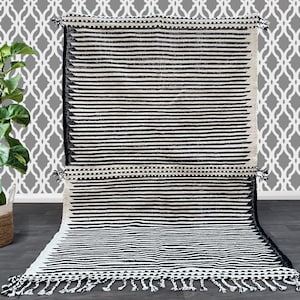 Handmade Moroccan striped rug crafted in wool, showcasing alternating black and white vertical lines (see photos). This minimalist design blends tradition with modern style, featuring fringed edges for artisanal charm. Durable, soft, and timeless, it’s the perfect accent for boho interiors, Scandinavian living rooms, or contemporary spaces seeking elegance with a touch of Moroccan heritage.
