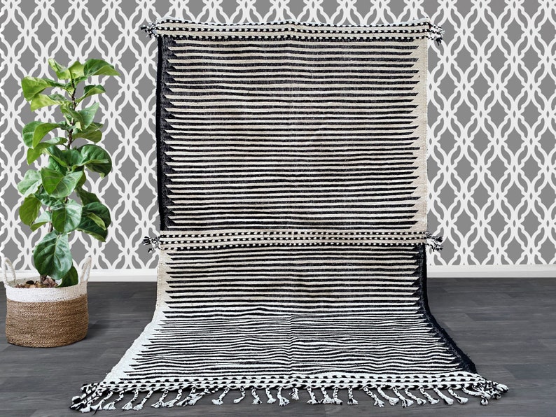 Handmade Moroccan striped rug crafted in wool, showcasing alternating black and white vertical lines (see photos). This minimalist design blends tradition with modern style, featuring fringed edges for artisanal charm. Durable, soft, and timeless, it’s the perfect accent for boho interiors, Scandinavian living rooms, or contemporary spaces seeking elegance with a touch of Moroccan heritage.