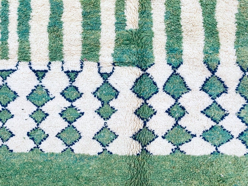 K&ouml;nnte beinhalten: Ein wei&szlig;er und gr&uuml;ner Teppich mit geometrischem Muster. Der Teppich hat einen Fransenrand und ist aus weichem, pl&uuml;schigem Material.