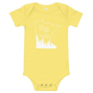 May include: A yellow baby bodysuit with short sleeves. The white graphic on the front features the outline of the state of Minnesota, the text "Oh Fer Cute", and a row of trees.