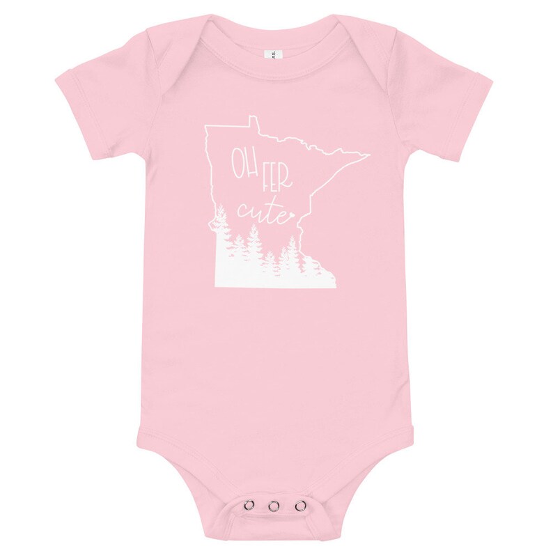 May include: A light pink baby bodysuit with short sleeves. The front features a white outline of the state of Minnesota with the words "Oh Fer Cute" and a forest silhouette inside the state outline.