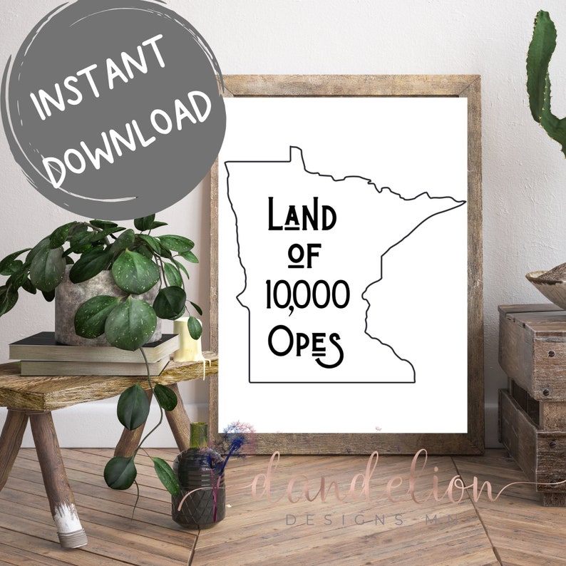 May include: A framed print with a black outline of Minnesota, displaying the text "Land of 10,000 Opes". The print is on a white background, framed in a light wood frame. The words "Instant Download" are in a grey circle. The print is a decorative item.