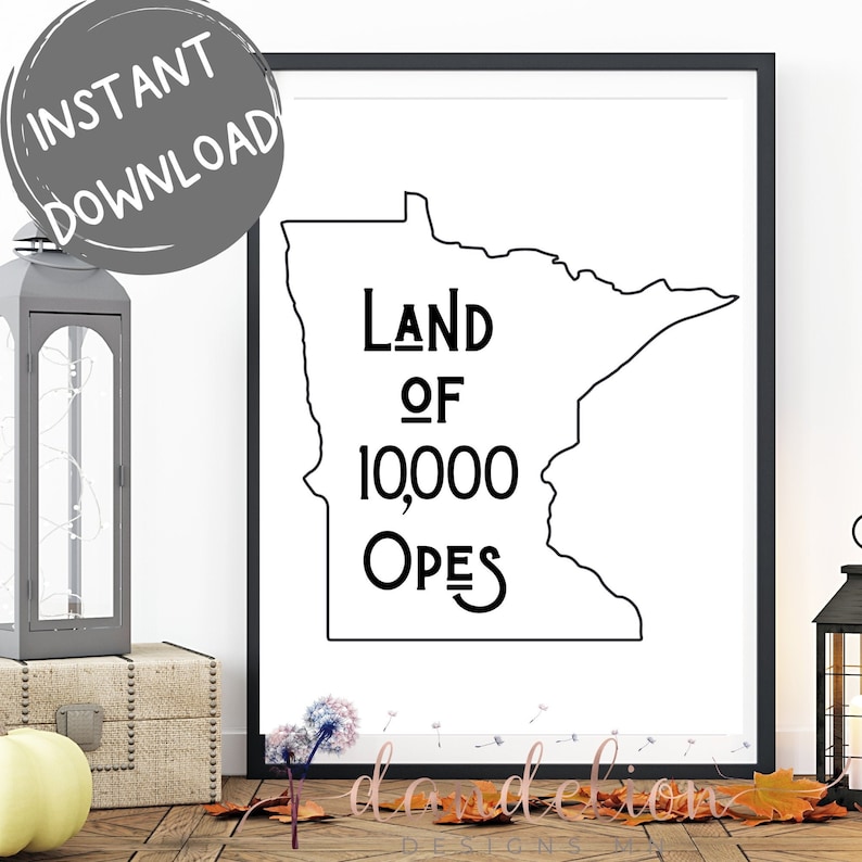 May include: A framed black and white print showing the outline of Minnesota. The text "Land of 10,000 Opes" is inside the state's borders. A grey circle with "Instant Download" is in the upper left. The print is displayed on a wooden surface.