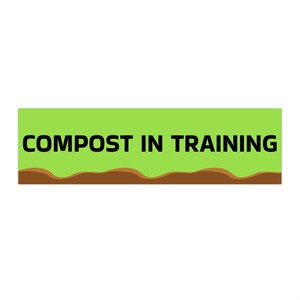 May include: A rectangular sign with a light green background and the words "COMPOST IN TRAINING" in bold black letters. A brown wavy line, representing soil, is at the bottom of the sign.