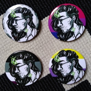 May include: Four round button badges featuring black and white illustrations of a person with long hair and glasses. Each badge has a different coloured background: black and white, pink, purple and yellow.