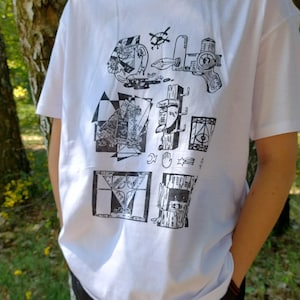May include: White t-shirt with a black graphic print. The print features various abstract illustrations, including geometric shapes, a gun, and other artistic elements. The shirt is short-sleeved and appears to be made of cotton.