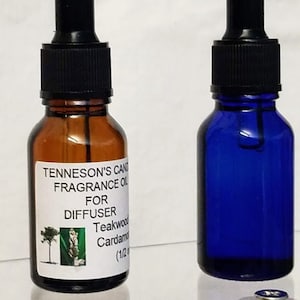 May include: Two glass bottles with droppers, one brown and one blue. The brown bottle has a label that reads "Tenneson's Candle Fragrance Oil for Diffuser Teakwood Cardamom (1/2 oz)".