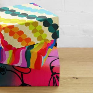 May include: Three gift boxes stacked on top of each other. The top box has a pattern of colourful circles and green circles. The middle box has a pattern of colourful wavy lines. The bottom box has a pink background with black flowers.