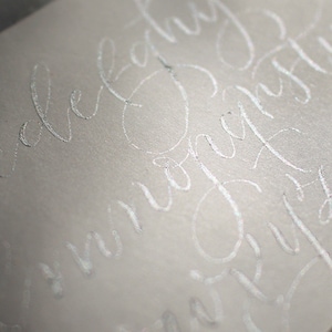 Pu&ograve; includere: Primo piano di una busta bianca con calligrafia argentata che recita "Ti amo per sempre" e "Congratulazioni".
