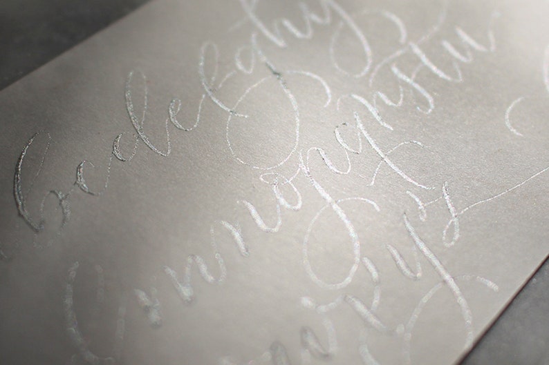Pu&ograve; includere: Primo piano di una busta bianca con calligrafia argentata che recita "Ti amo per sempre" e "Congratulazioni".