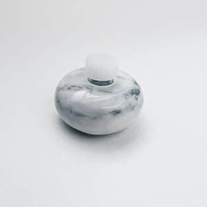 May include: White marble bottle with a white plastic lid. The bottle has a smooth, rounded shape and a marbled pattern.