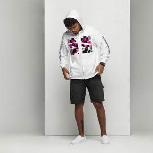 May include: White zip-up hoodie with a pink and black graphic design on the front. The hoodie has a hood with a drawstring and long sleeves. The model is wearing black shorts.