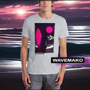 Puede incluir: Una camiseta gris con un estampado gráfico de una persona de pie en una playa con una tabla de surf y una luna rosa en el fondo. El texto "WAVEMAKO" está impreso en la parte inferior del gráfico.