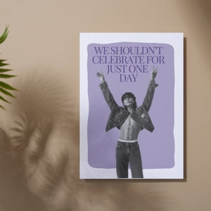 May include: A poster with a lilac background and the text "WE SHOULDN'T CELEBRATE FOR JUST ONE DAY." The poster features a black and white image of a person wearing a denim jacket and jeans with arms raised. The background is a neutral beige.