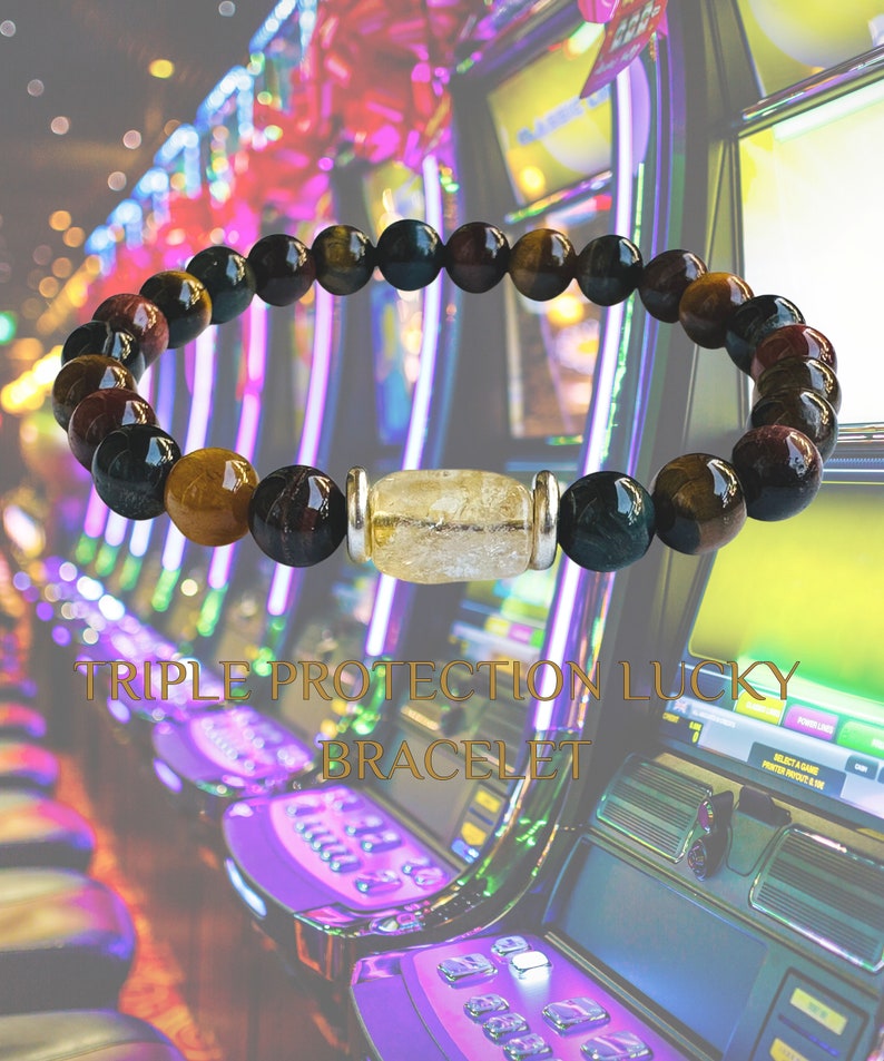 K&ouml;nnte beinhalten: Ein dreifach sch&uuml;tzendes Gl&uuml;cksarmband mit schwarzen, braunen und gr&uuml;nen Perlen und einer klaren Quarzperle mit silbernen Akzenten. Das Armband ist vor einer Reihe von Spielautomaten fotografiert.