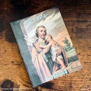 May include: A religious booklet featuring an illustration of Saint Joseph holding a child, with the text "NOVENA" at the top and "SAN JOSE" at the bottom. The image has a vintage aesthetic, with soft colors and a weathered appearance.