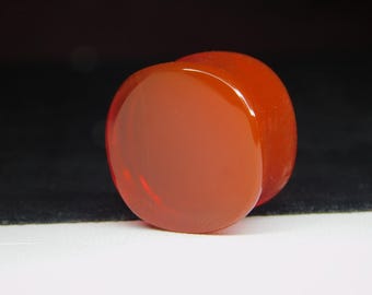 May include: A close-up of a rounded, orange-red object with a glossy surface. The object is set against a black and white background, highlighting its smooth texture and color. The shape is reminiscent of a smooth stone or a polished gem.