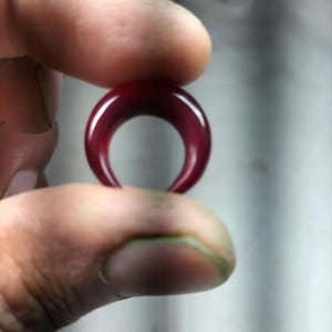 Peut inclure: Un bijou en forme de croissant de lune de couleur rouge foncé, probablement un anneau de septum ou un anneau de nez.