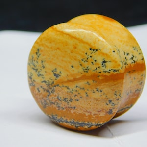 May include: A round, yellow and brown stone with black flecks. The stone has a smooth, polished surface.