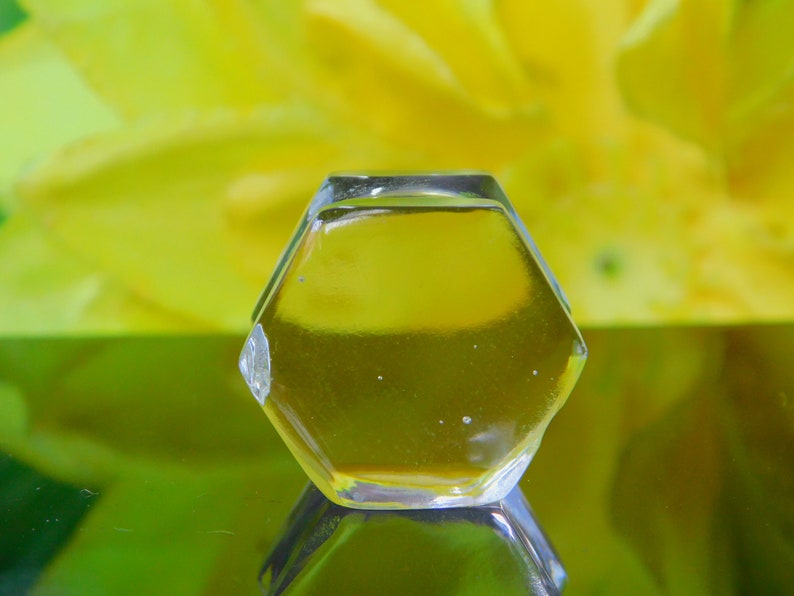 May include: A clear glass hexagonal bottle stopper with a yellow liquid inside. The bottle stopper is sitting on a reflective surface.