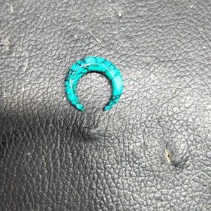 Peut inclure: Une boucle d'oreille en forme de fer à cheval turquoise et noire. La boucle d'oreille est faite d'un matériau lisse et poli.