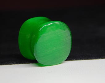 May include: A vibrant green ear plug with a smooth, polished surface. The plug has a rounded, cylindrical shape with a flat, circular face. The color is a bright, saturated green, and the material appears to be glossy.