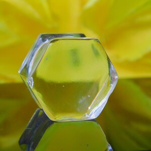 May include: A clear, hexagonal glass ice cube sits on a yellow reflective surface.
