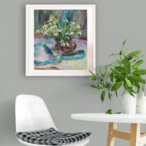 May include: A framed oil painting depicts a still life of white flowers in a brown vase, with a blue ribbon. The painting is set against a neutral background. A white chair with a checkered cushion and a small white table are in the foreground.