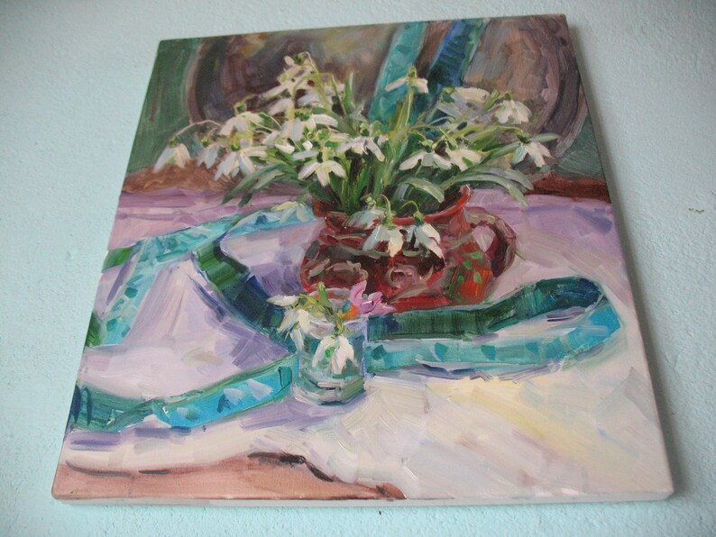 May include: An oil painting depicts a still life with white snowdrop flowers in a red ceramic pitcher and a small glass. A teal ribbon is draped across the white tablecloth. The background features muted brown tones.