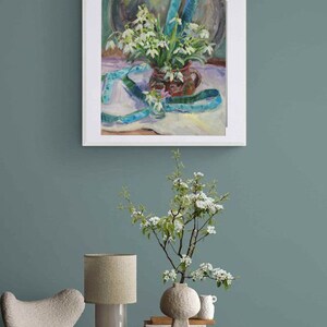May include: An oil painting of a still life featuring a bouquet of white flowers in a brown vase, accented with a blue ribbon. The painting is framed and hangs on a teal wall. A side table holds a lamp, vase, and books.