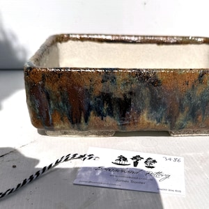May include: A rectangular ceramic bonsai pot with a brown, blue and white glaze. The pot has a square base and a slightly flared rim.