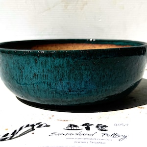 May include: A teal ceramic bowl with a textured finish. The bowl has a wide, shallow design with a dark interior. The Samarkhand Pottery logo is visible at the bottom. This decorative bowl is suitable for serving or display.