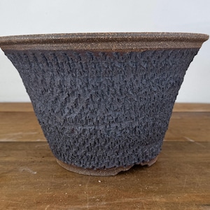 May include: A wide, conical ceramic planter featuring a dark, charcoal-coloured exterior with a deeply textured, crinkled surface. The rim and the base of the vessel are finished in a contrasting, smooth, earthy brown clay tone.