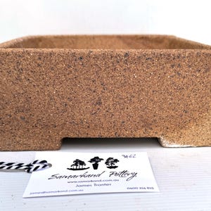 May include: A rectangular, textured, brown ceramic planter with a square opening. The planter has a slightly rough surface and sits on a white surface. A tag with the text "Samarkand Pottery" is attached to the planter.