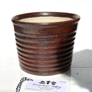May include: A brown ceramic pot with a ribbed design. The pot is handmade and has a rustic look. The pot is labelled "Samarkand Pottery" and "James Tranter".