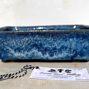 May include: A rectangular ceramic bonsai pot with a deep blue glaze featuring mottled white and light blue textures. A white rectangular tag is attached by a black and white string, displaying the text Samarkand Pottery, a website, and contact details.