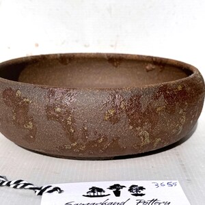 May include: A brown ceramic bonsai pot with a rough, textured surface. The pot has a wide, shallow shape and a slightly rounded bottom.