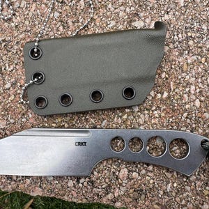 May include: A silver CRKT knife with a straight edge and multiple circular cutouts, paired with an olive green sheath. The knife has a lanyard attached. The sheath has a chain for carrying.