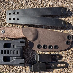 May include: A selection of tactical equipment, including a brown knife sheath, a tan knife, black belt loops, and a black mounting system. The knife has a textured handle. The sheath has multiple eyelets.