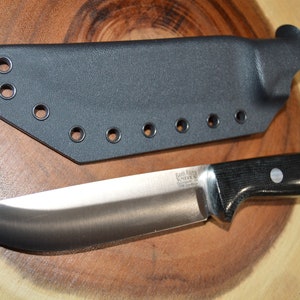May include: A black leather knife sheath with multiple belt loops and a black handled knife with a silver blade. The knife has a black and white patterned handle with a silver logo that reads "Bark River Knives".