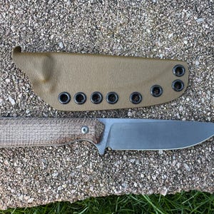 Peut inclure: Un couteau &agrave; lame fixe avec un manche textur&eacute; et une lame argent&eacute;e, accompagn&eacute; d'un &eacute;tui beige. L'&eacute;tui comporte plusieurs &oelig;illets. Le couteau et l'&eacute;tui sont pr&eacute;sent&eacute;s sur une surface textur&eacute;e semblable &agrave; de la pierre.