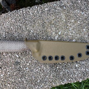 Peut inclure: Un couteau &agrave; lame fixe avec un manche beige et un &eacute;tui assorti. L'&eacute;tui comporte des &oelig;illets noirs le long du bord. Le manche du couteau a une texture tiss&eacute;e. Le couteau est con&ccedil;u pour une utilisation en ext&eacute;rieur.