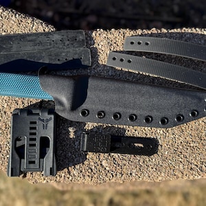 Peut inclure: Un étui à couteau noir avec un couteau bleu et noir à l'intérieur. L'étui comporte plusieurs rangées d'œillets et une sangle noire. Il y a un porte-couteau en plastique noir et deux sangles noires avec des boutons-pression métalliques.