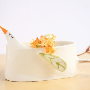 A close-up shot of the white ceramic bird planter on a light wood surface against a plain white background.