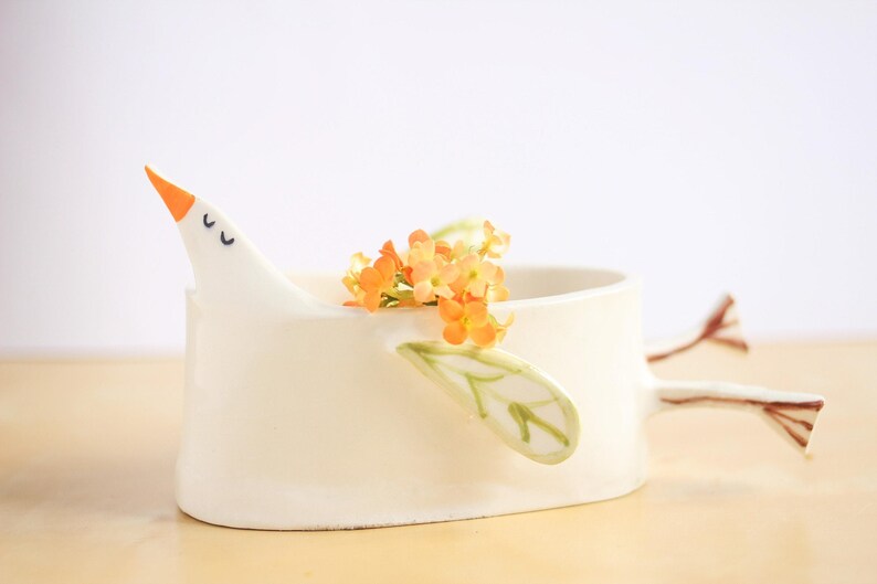 A close-up shot of the white ceramic bird planter on a light wood surface against a plain white background.