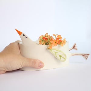 A hand gently supports the white ceramic bird planter against a plain white background.