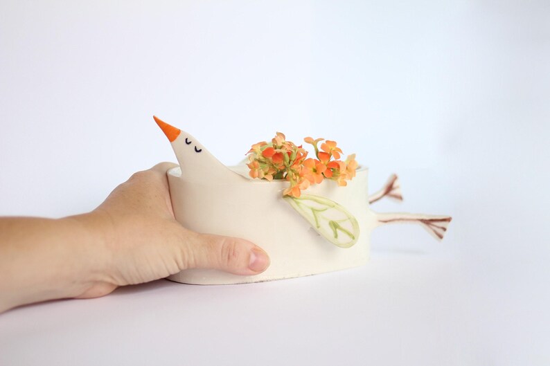 A hand gently supports the white ceramic bird planter against a plain white background.