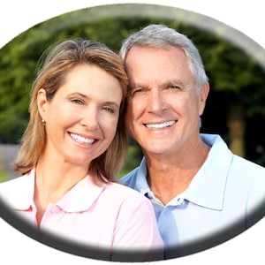 May include: A smiling couple poses for a photo outdoors. The woman is wearing a pink polo shirt and the man is wearing a light blue polo shirt.