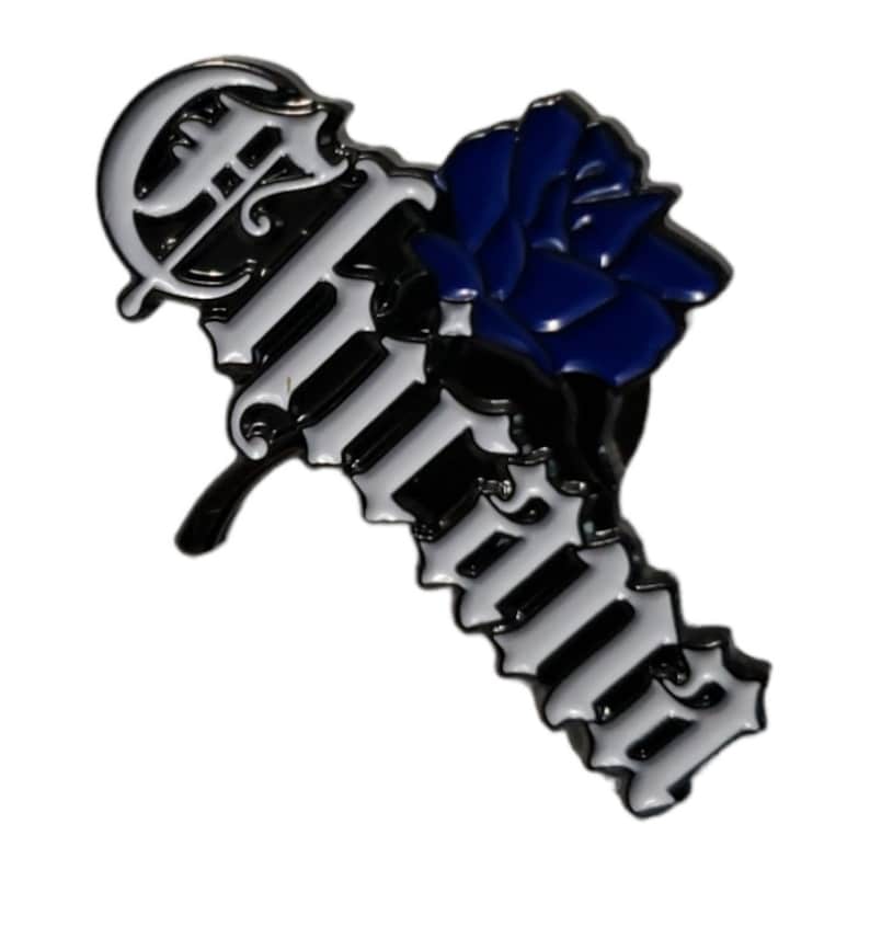 May include: A black and white enamel pin with the word "Forever" in a gothic font. A blue rose is on the left side of the pin.